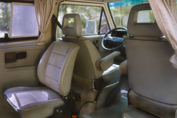 Spacious and comfortable RV rental interior, showing a light gray passenger seat with armrest and the driver's area.. Volkswagen Westfalia 1990