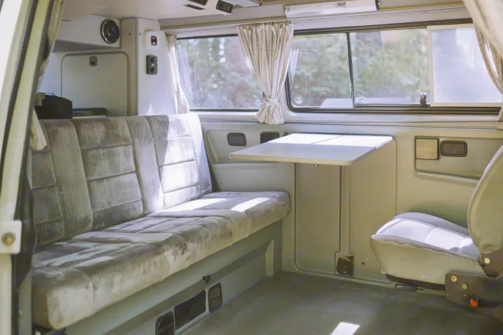 Cozy RV rental interior with bench seating, a retractable table, and large windows, ready for travel adventures.. Volkswagen Westfalia 1990