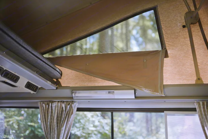 Inside an RV rental camper: a raised pop-top tent with a mesh window views of trees, and a lower window with curtains.. Volkswagen Westfalia 1990