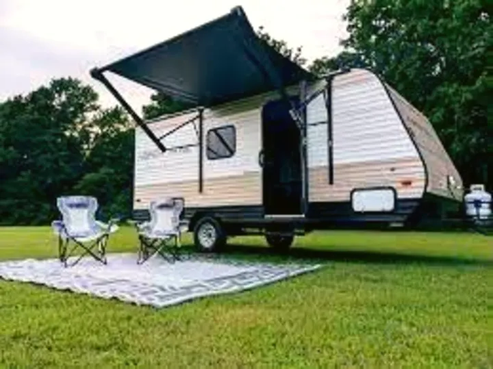 This RV rental is ready! A travel trailer with an awning, chairs & mat on green grass for outdoor camping.. Aspen Trail 17BH 2021