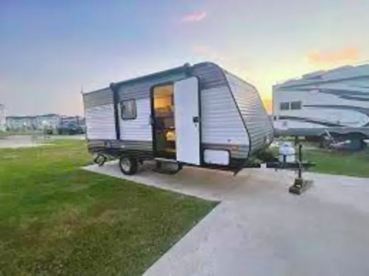 A gray and black RV rental travel trailer with its door open sits on a paved campsite at dusk. Ideal for your next outdoor escape.. Aspen Trail 17BH 2021