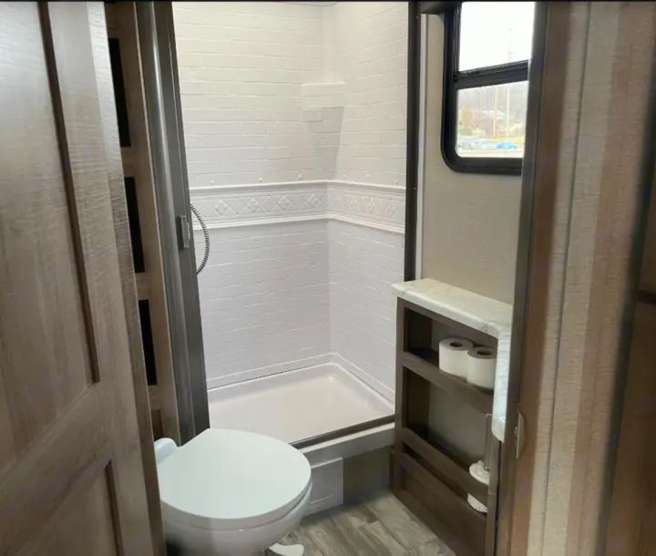 View inside a clean RV rental bathroom, featuring a shower, toilet, and practical built-in shelving.. Grand Design Imagine XLS 2021