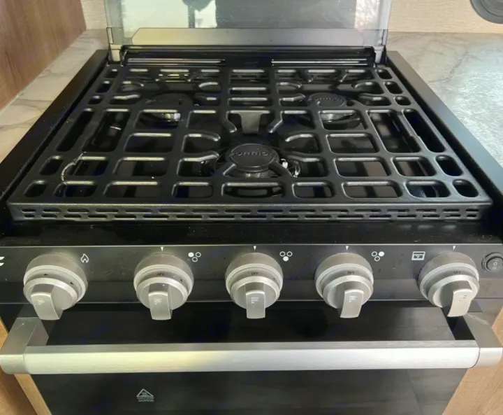 Compact gas range and oven in an RV rental. Features black stovetop grates, burner controls, and a silver oven handle.. Grand Design Imagine XLS 2021