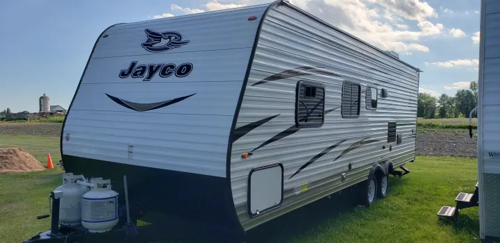 Jayco travel trailer, a white and grey RV rental with propane tanks, parked on grass for outdoor trips.. Jayco Jay Flight SLX 2018