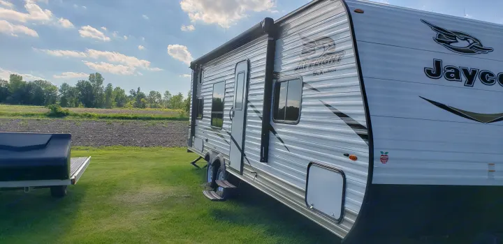 Jayco travel trailer RV rental beside a tilled field under a bright, cloudy sky. Perfect for an outdoor getaway.. Jayco Jay Flight SLX 2018