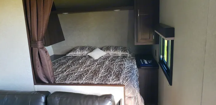 RV rental interior: cozy bedroom with patterned bed, brown curtains, and storage cabinet.. Jayco Jay Flight SLX 2018