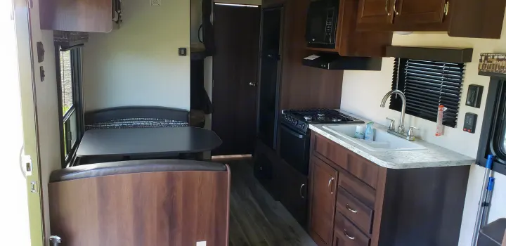Inside an RV rental: a compact kitchen with stove, sink, and microwave, opposite a cozy dinette with table and bench seats.. Jayco Jay Flight SLX 2018