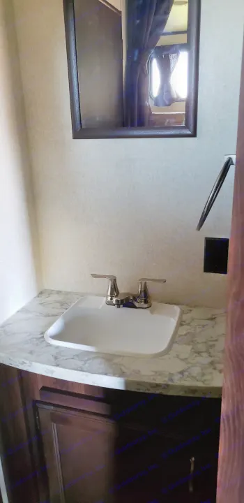Compact RV rental vanity featuring a white sink, marble countertop, and mirror reflecting a window with curtains.. Jayco Jay Flight SLX 2018