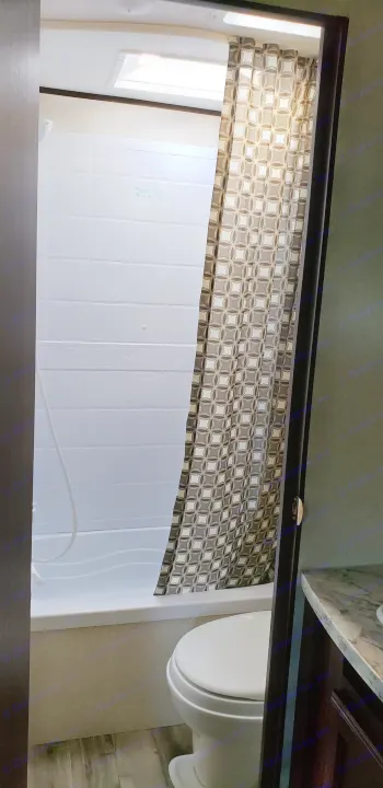 Compact RV rental bathroom with white tiled shower/tub, patterned curtain, and toilet visible.. Jayco Jay Flight SLX 2018