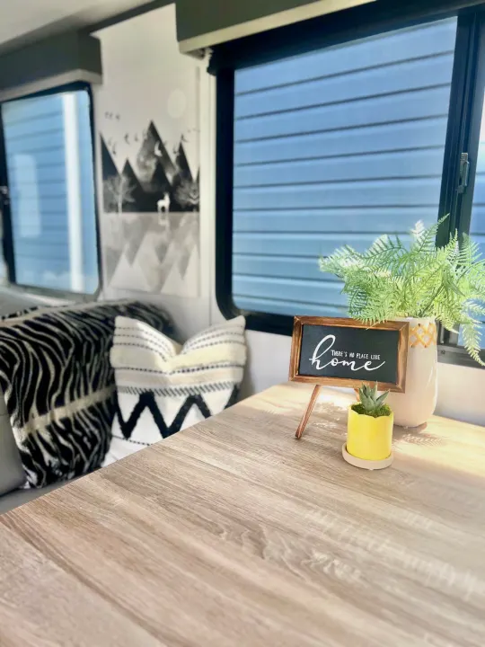 Step into this stylish RV rental! Featuring a light wood table, "home" sign, plants, and cozy seating with pillows.. Keystone Bullet Ultra Lite 2023