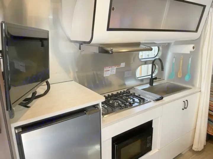 Bright, compact RV rental kitchen with sink, gas stove, microwave, fridge, TV, and signature oval windows.. Airstream Caraval 2021