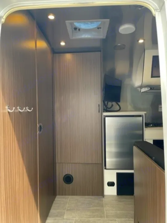 Inside a functional RV rental: view of its compact living space with stainless steel fridge, mounted TV, and storage cabinetry.. Airstream Caraval 2021
