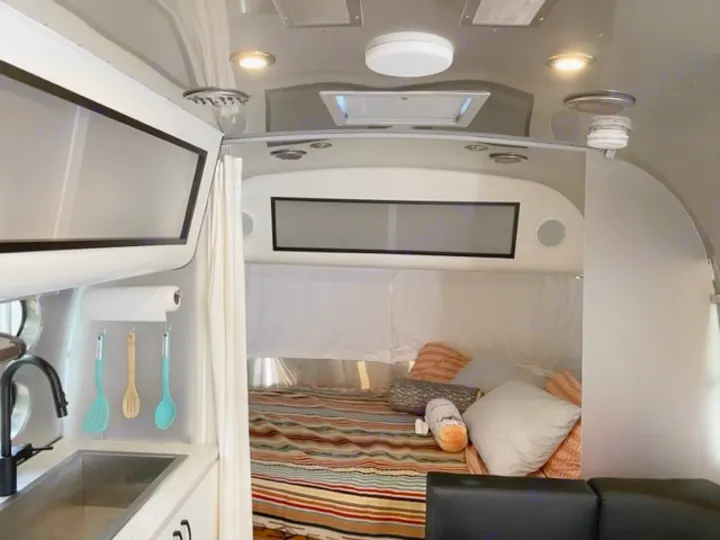 Inside a modern **rv rental**, featuring a compact kitchen with a sink & utensils, a comfy bed, and seating area.. Airstream Caraval 2021