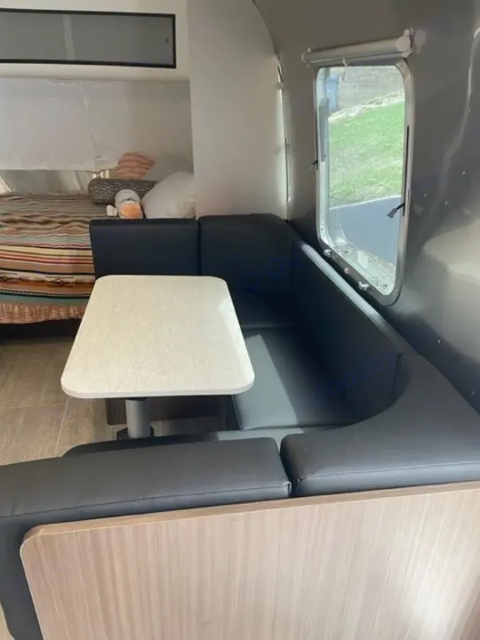 Modern RV rental interior: cozy dinette with black seating and table, plus a comfortable bed.. Airstream Caraval 2021