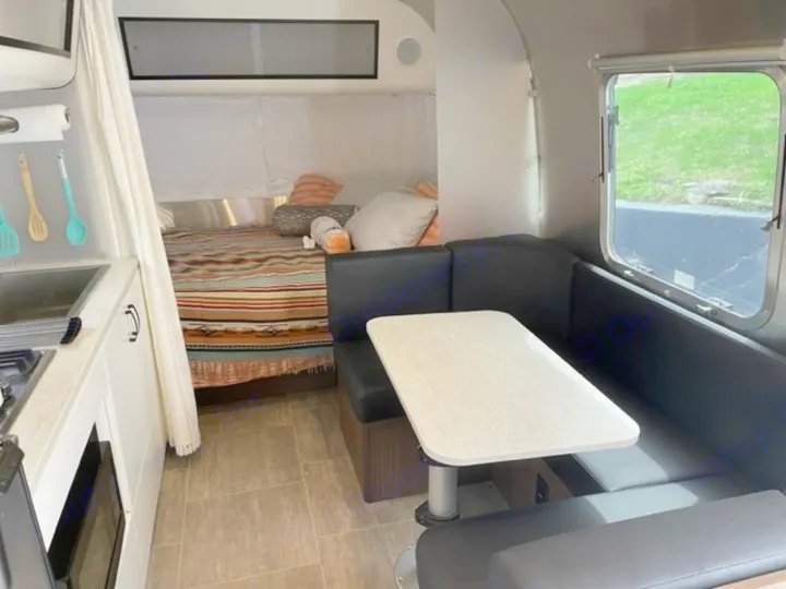 Explore this RV rental's cozy interior: a compact kitchen, bed with patterned blanket, and black dinette with a table by a window.. Airstream Caraval 2021