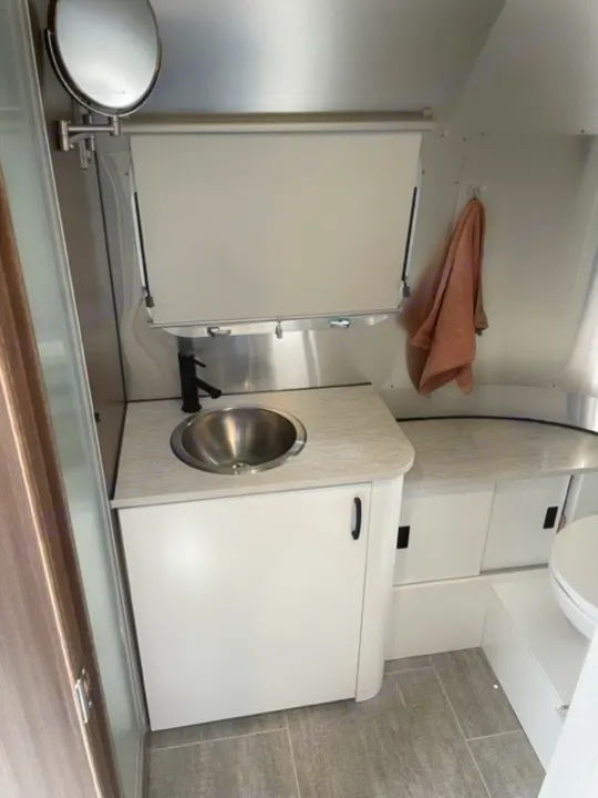 Compact RV rental bathroom with stainless steel sink, mirror, and storage. Ideal for travel comfort.. Airstream Caraval 2021