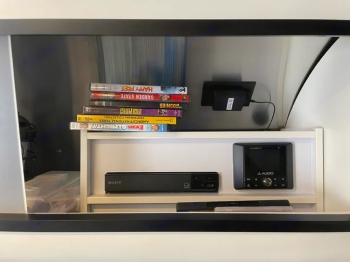 An RV rental entertainment console with a stack of DVDs, a Sony Blu-ray player, and a JL Audio marine stereo.. Airstream Caraval 2021