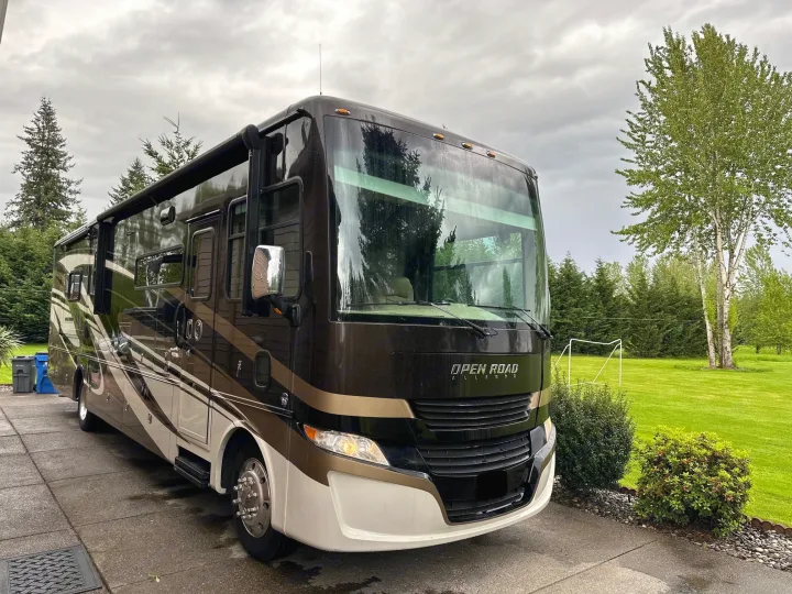 Large dark motorhome, perfect for an RV rental, parked on a driveway next to a lush green lawn and trees.. Allegro Allegro Open Road 2019