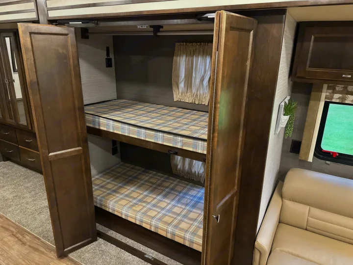 Inside an RV rental: dark wood bunk beds with plaid mattresses are revealed from a cabinet. A compact and functional sleeping area.. Allegro Allegro Open Road 2019
