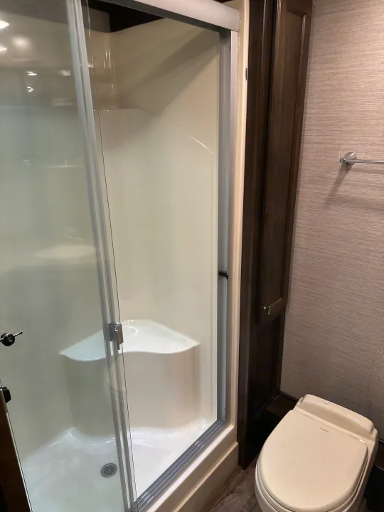 RV rental bathroom featuring a spacious shower with clear glass doors and a Dometic toilet, complemented by dark wood trim.. Allegro Allegro Open Road 2019