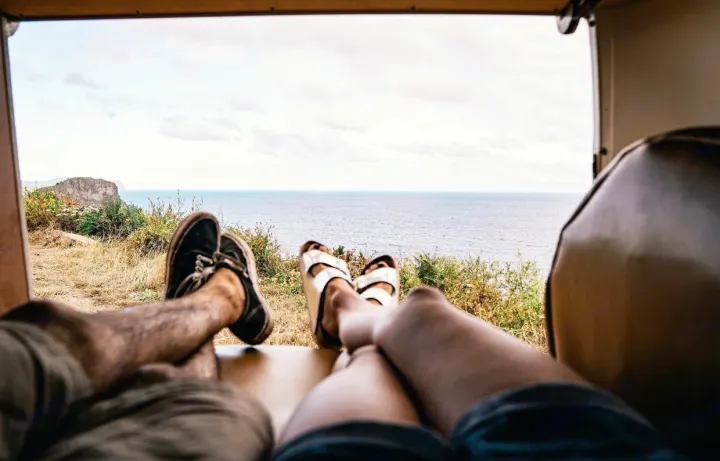 Relaxing RV rental: A couple's feet propped up inside a van, enjoying a beautiful ocean and cliff view.. Volkswagen T2 Westfalia 1971