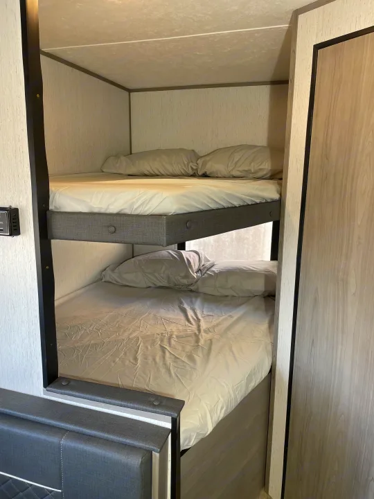Explore this RV rental's cozy bunk beds, complete with light bedding and upholstered frames, offering comfortable sleeping for your trip.. Dutchmen Coleman Lantern LT 2022