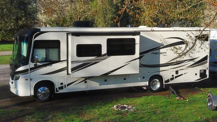 This Jayco Precept Class A RV rental is parked outdoors with its awning extended, ready for camping near a small fire pit.. Jayco Precept 2021