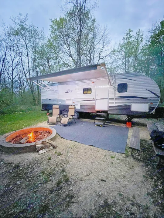 Enjoying a cozy RV rental campsite with a fire pit, chairs, and extended awning, surrounded by nature.. Crossroads RV Z-1 2017