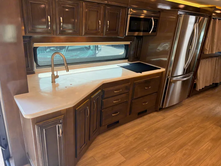 Modern RV kitchen in an rv rental, featuring dark wood cabinets, light countertops, sink, microwave, and large stainless fridge.. Entegra Coach Accolade XL 37L  Super-C 2023