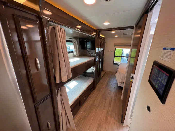 Inside this RV rental: spacious interior with dark wood bunk beds, privacy curtains, and a bright hallway leading to more sleeping areas.. Entegra Coach Accolade XL 37L  Super-C 2023