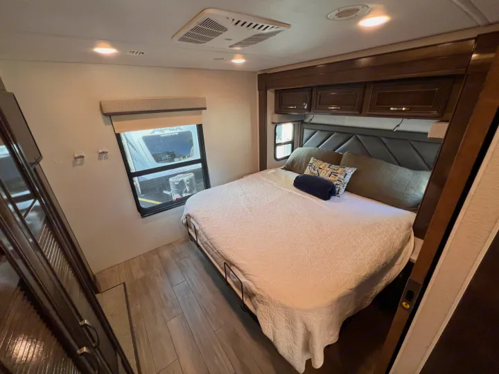Cozy RV rental bedroom with comfortable bed, overhead cabinets, and window views showing other RVs.. Entegra Coach Accolade XL 37L  Super-C 2023
