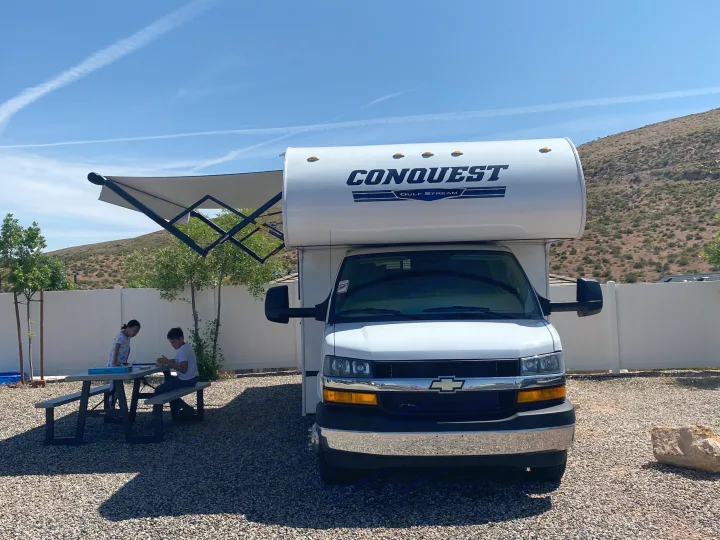 RV rental vacation: Kids enjoy playing games at a picnic table by their Conquest Gulf Stream motorhome under a sunny sky.. Gulf Stream Conquest 6280LE 2023