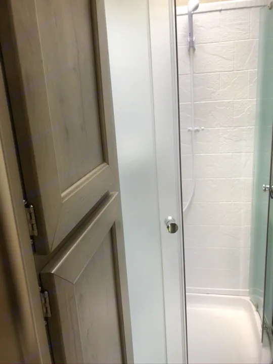 Compact RV rental features a light-wood cabinet next to a clear glass shower with white tiled walls and showerhead.. Forest River Palomino Puma XLE Toy Hauler 2019