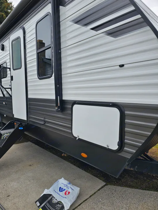 RV rental: Open exterior storage compartment on a white and grey striped travel trailer, showing its practical side.. Highland Ridge RV Olympia 2022