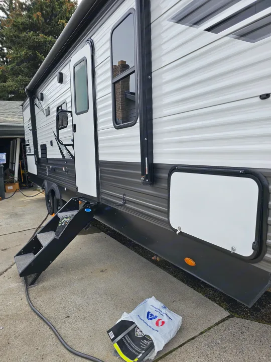 An RV rental with its side steps deployed, parked on concrete. Features windows and a patio mat for camping.. Highland Ridge RV Olympia 2022