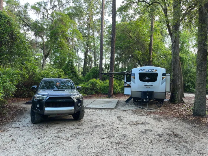 An RV rental and Toyota 4Runner are parked at a spacious, tree-filled campsite, ready for an outdoor adventure.. Forest River Rockwood Geo Pro 2020