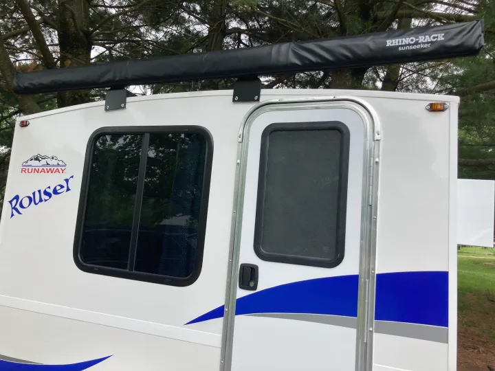 White Runaway Rouser RV rental showing its side profile with an attached Rhino-Rack awning, window, and door. Ready for travel.. Runaway Rouser 2023