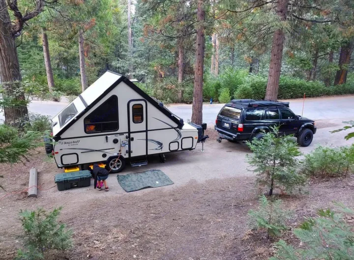 RV rental: An A-frame camper and SUV are parked at a wooded campsite, ready for an outdoor adventure.. Forest River Flagstaff Classic 2019