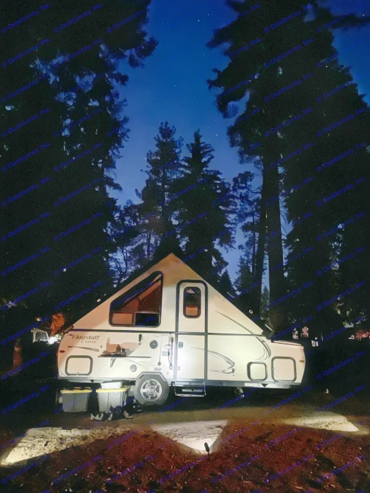 Lit A-frame RV rental parked at night under a starry sky, surrounded by dark trees.. Forest River Flagstaff Classic 2019