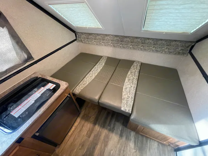 Compact RV rental interior showing a gray dinette with patterned cushions, kitchen area with stovetop, and overhead skylights.. Forest River Flagstaff Classic 2019