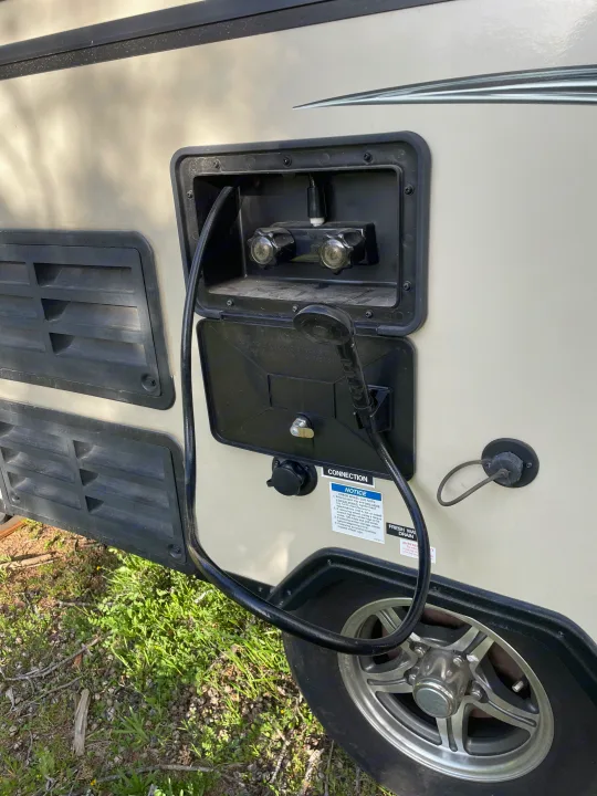 RV rental exterior showing the outdoor shower and water hookup, with utility access panels and a wheel.. Forest River Flagstaff Classic 2019