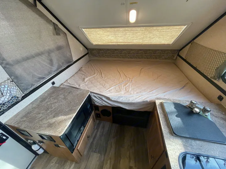 This compact RV rental interior features a bed, kitchenette with microwave & sink, and overhead light.. Forest River Flagstaff Classic 2019
