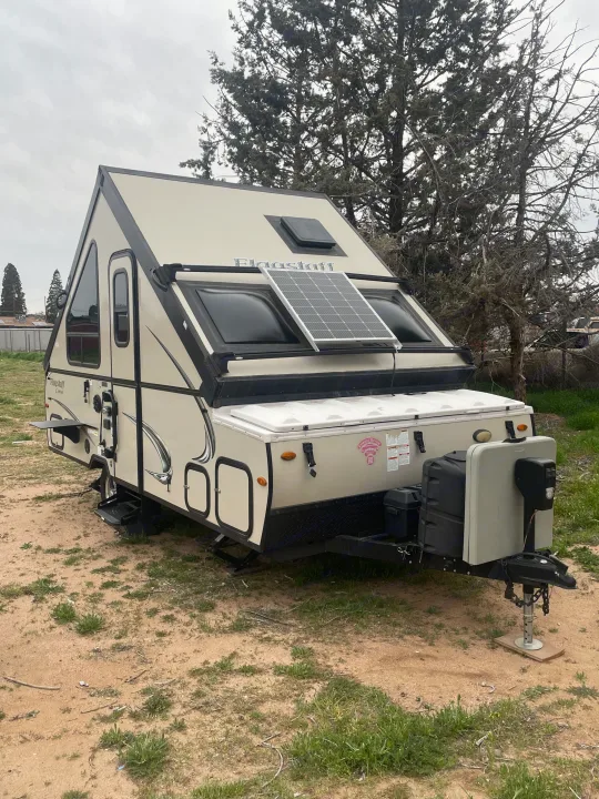 A beige Flagstaff A-frame pop-up camper with a solar panel, parked on dirt, ready as an rv rental.. Forest River Flagstaff Classic 2019