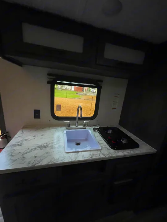 An RV rental kitchen featuring a white sink, silver faucet, black stove, and marble-patterned countertop. Ready for your adventure!. Dutchmen Aspen Trail 2023