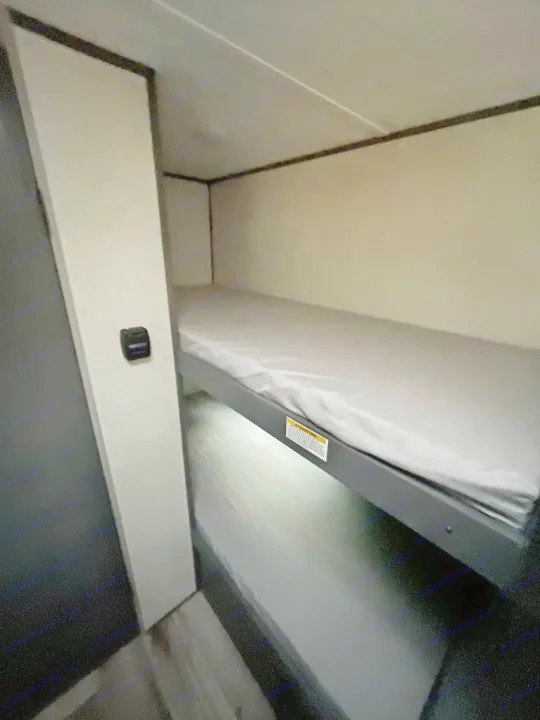 Cozy RV rental bunk beds offer comfy sleeping. Top bunk has a warning label; bottom bunk is visible below.. Dutchmen Aspen Trail 2023