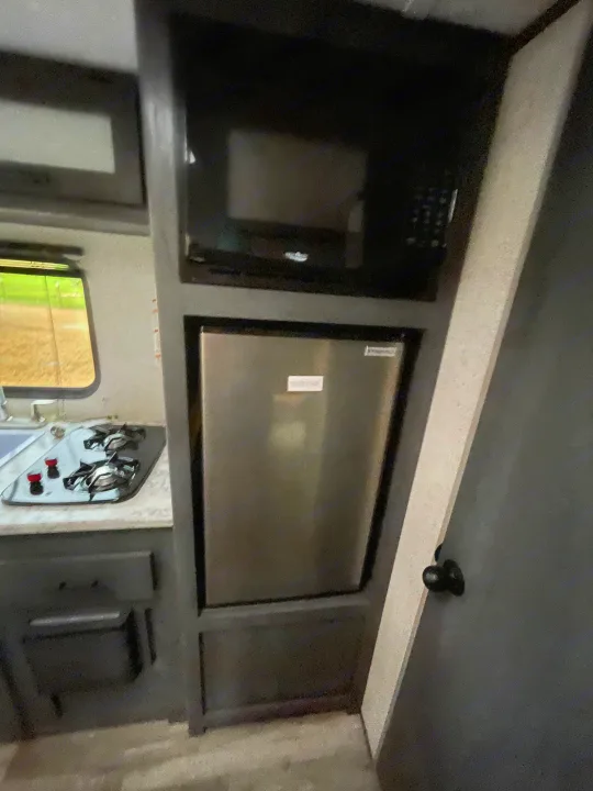 Compact RV rental kitchen featuring microwave, fridge, and two-burner stove.. Dutchmen Aspen Trail 2023