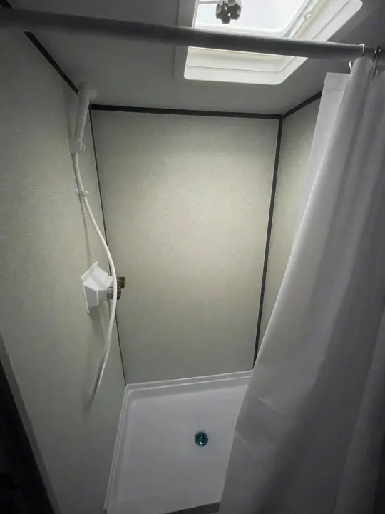 Step inside this RV rental shower: compact with a handheld showerhead, curtain, and ceiling vent, perfect for travel.. Dutchmen Aspen Trail 2023