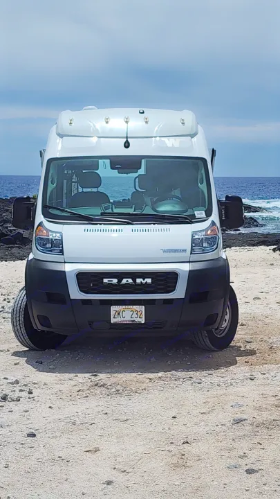 White Ram Promaster RV rental on a gravel path near the ocean.. Winnebago Solis 2023