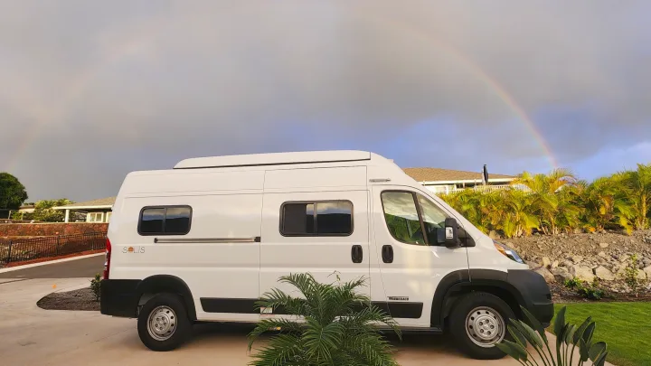 White Winnebago Solis RV rental parked outdoors, with a vibrant rainbow arching across the cloudy sky. Perfect for travel!. Winnebago Solis 2023