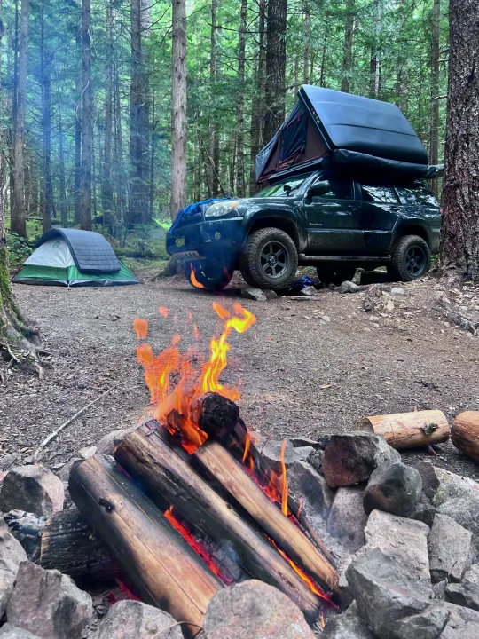 Forest camping setup with a roaring campfire, ground tent, and rooftop tent car. Perfect overlanding adventure, like an RV rental!. Toyota 4runner 2006